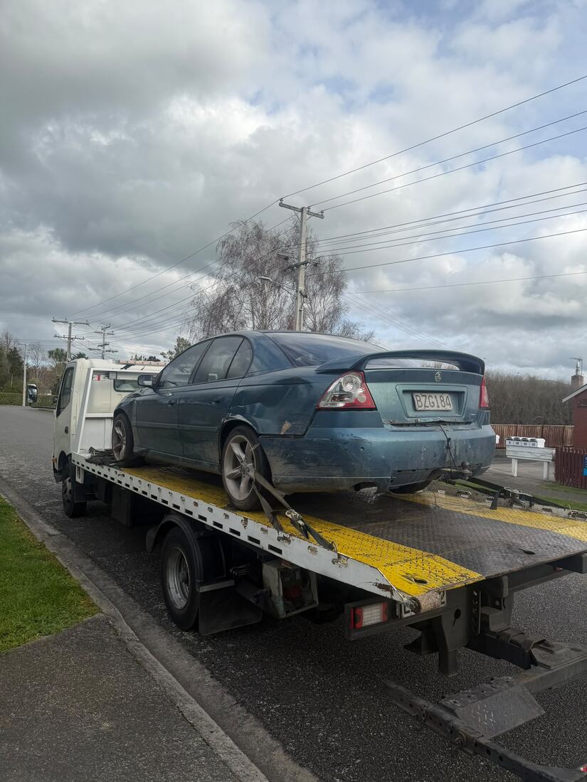 Blue Holden Commodore strapped onto a Cash For Cars Whakatāne tow truck