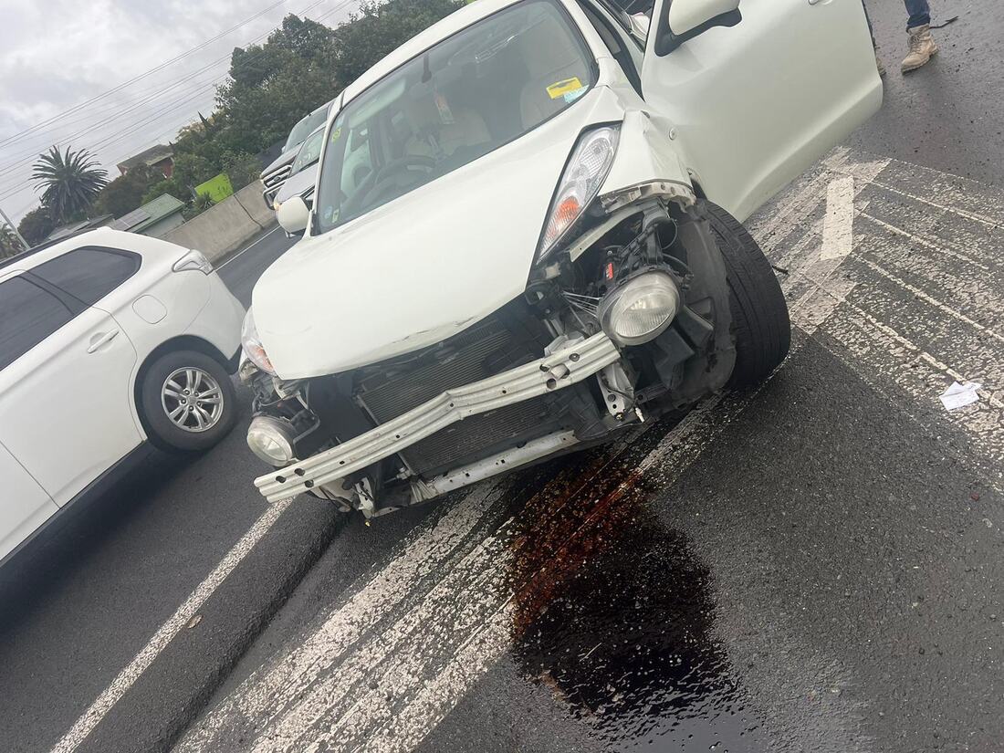 Dead white hatchback with a smashed front end and fluid leaking on the road
